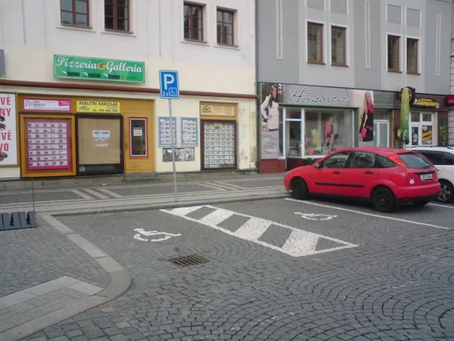 Červené auto zaparkované na ulici před obchody