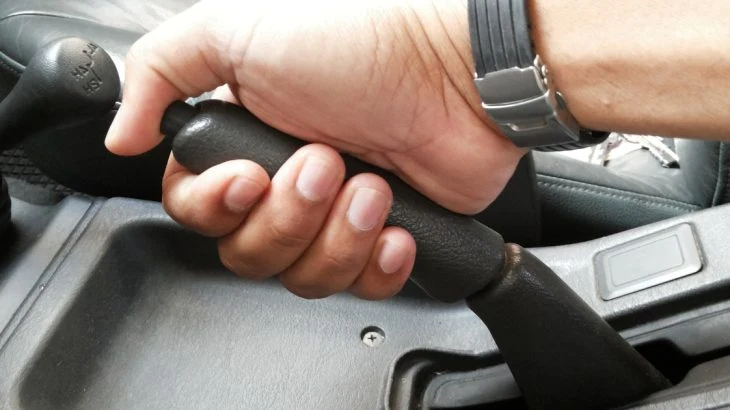 Ruka drží páku ruční brzdy v automobilu s automatikou.