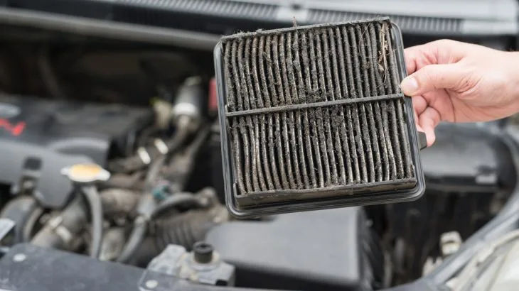 Zanesený vzduchový filtr držený nad otevřeným motorem.