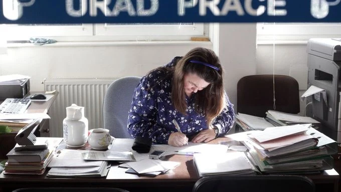 Žena pracuje v kanceláři s dokumenty na stole.