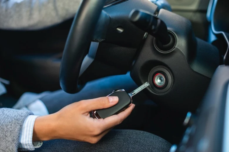 Ruka vkládá klíč do zapalování automobilu pro spouštění motoru.