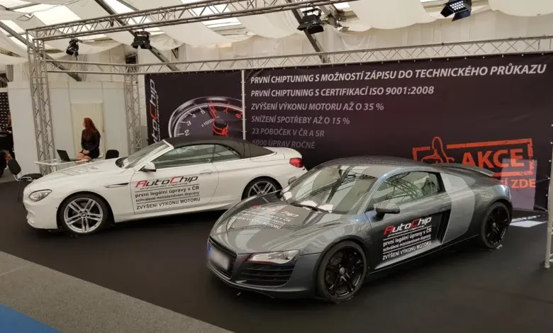 Dva upravené sportovní vozy na výstavě s reklamou na čipování motorů.