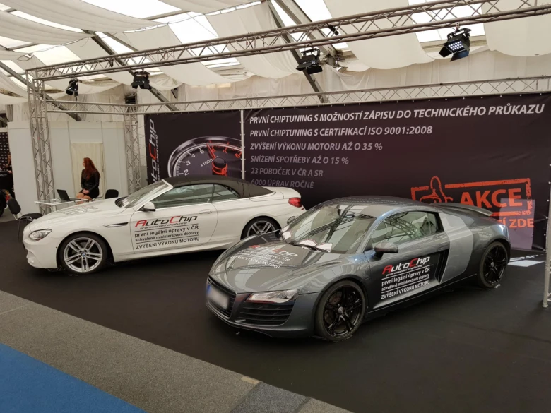 Dva upravené sportovní vozy na výstavě s reklamou na čipování motorů.