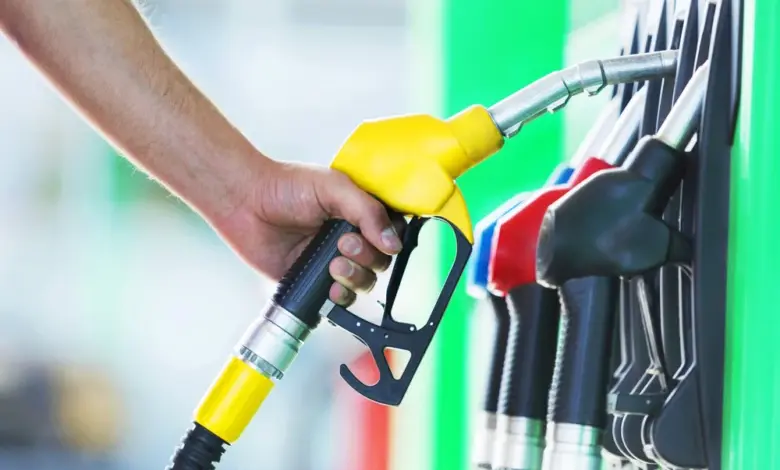 Ruka drží žlutou benzínovou čerpadlovku na zeleném čerpacím stanovišti.