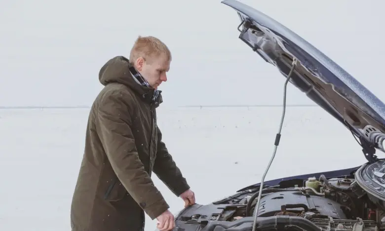 Muž kontroluje motor auta se zvednutou kapotou ve sněhu.