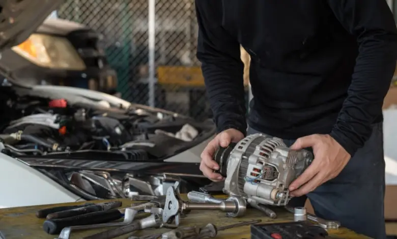 Mechanik drží automobilový alternátor u otevřeného motoru auta.