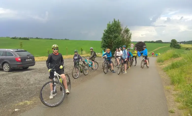 Skupina cyklistů na silnici vedle zelených polí s autem.