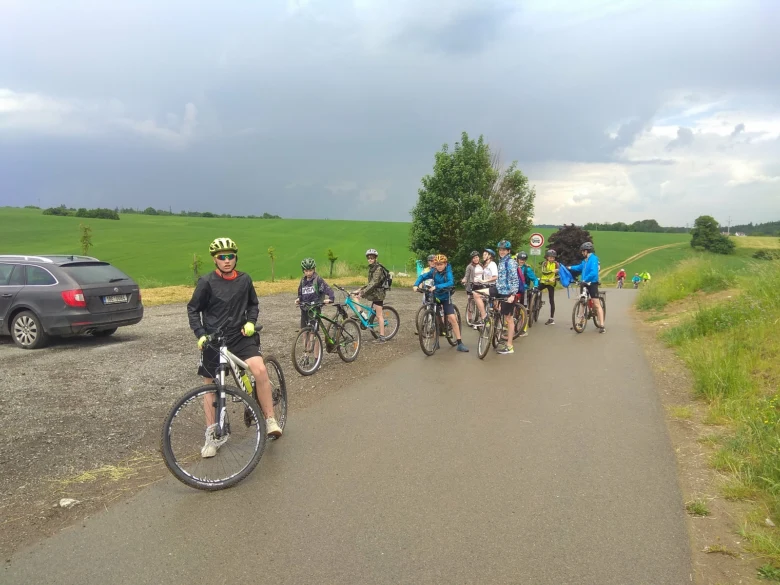 Skupina cyklistů na silnici vedle zelených polí s autem.