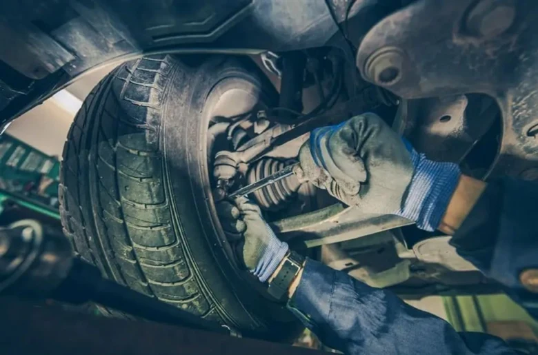 Mechanik opravuje vzpěru stabilizátoru pod kolou auta.