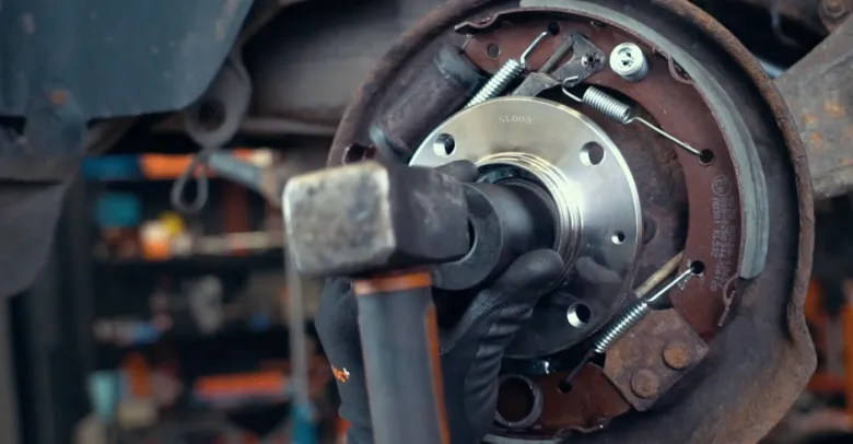 Mechanik opravuje ložisko kola pomocí kladiva uvnitř brzdového bubnu.