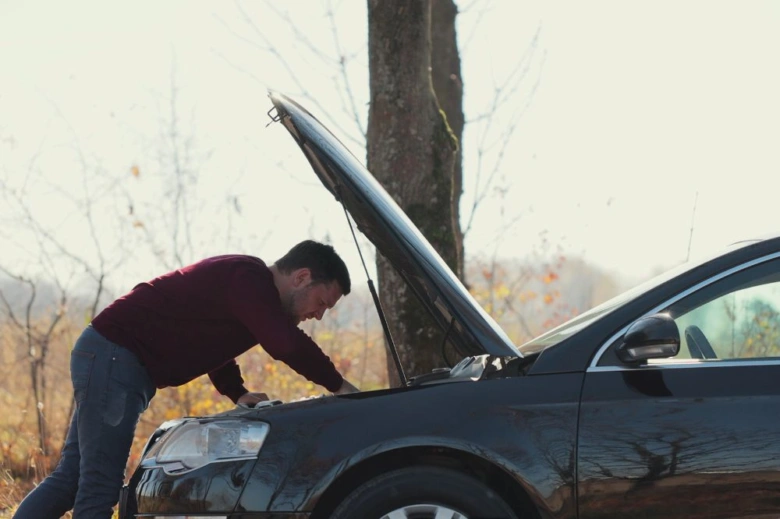 Muž kontroluje motor vozu s otevřenou motorkovou kapotou venku.