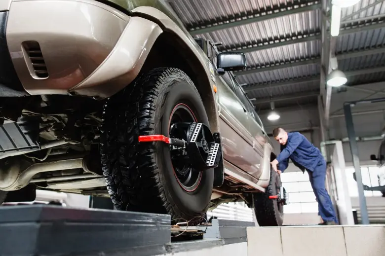 Mechanik upravuje geometrii kol automobilu na zvedáku v dílně.