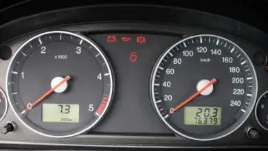 Vozidlový přístrojový panel s rozsvícenou kontrolkou ruční brzdy.