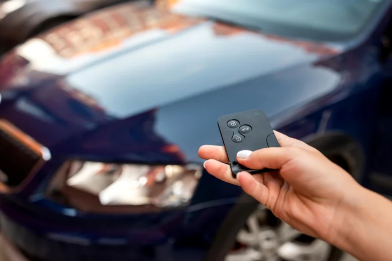 Člověk drží klíč auto s dálkovým ovládáním u modrého vozu.