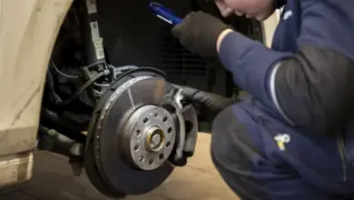 Mechanik kontroluje opotřebení brzdového kotouče s baterkou.