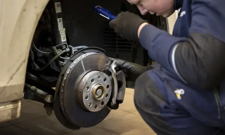 Mechanik kontroluje opotřebení brzdového kotouče s baterkou.