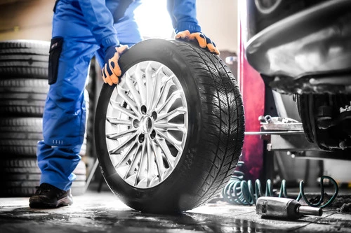 Mechanik montuje nové kolo na automobil v dílně.