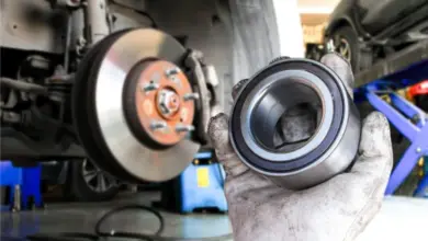 Mechanik drží poškozené ložisko kola s viditelnými známkami opotřebení.