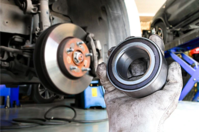 Mechanik drží poškozené ložisko kola s viditelnými známkami opotřebení.