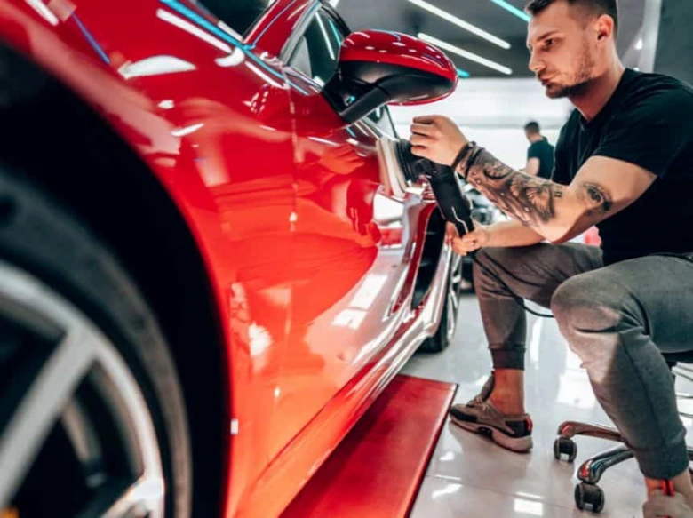 Muž aplikuje ochranný povlak na červené auto v dílně.