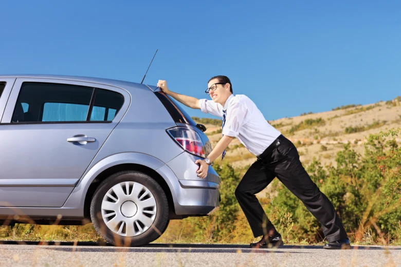 Muž tlačí stříbrné auto na silnici.