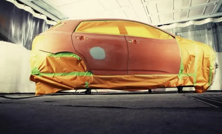 Červené auto připravené na lakování s maskováním v barvnickém boxu.
