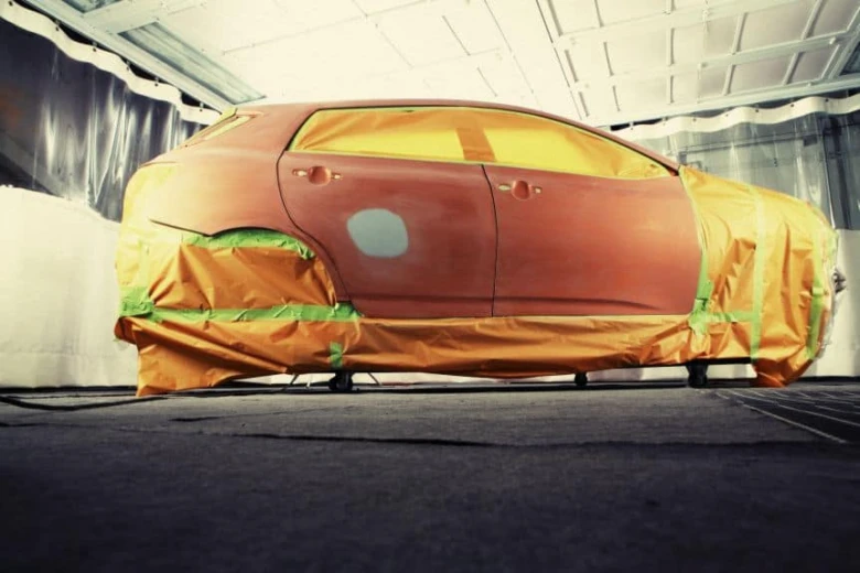 Červené auto připravené na lakování s maskováním v barvnickém boxu.
