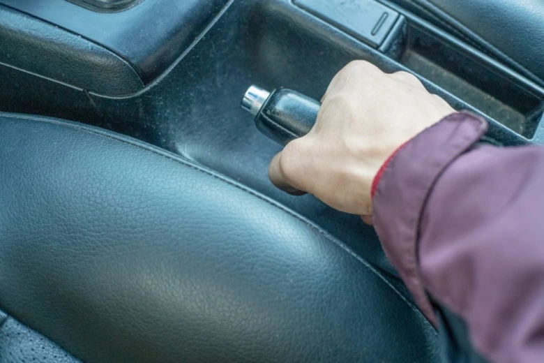 Ruka drží ruční brzdu v automobilu s automatickým převodovkou.
