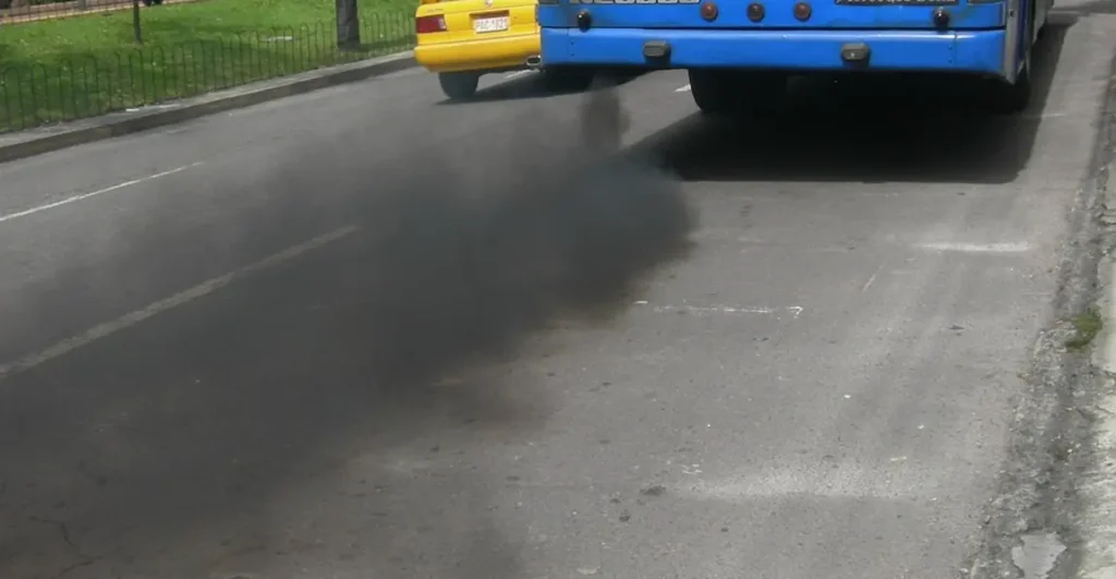 Modrý autobus kouří černým dymem při zrychlení na silnici.