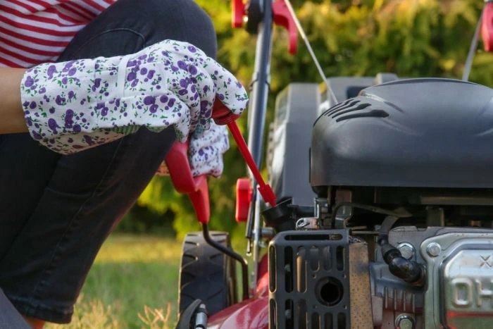 Osoba kontroluje hladinu oleje v sekačce na trávu.