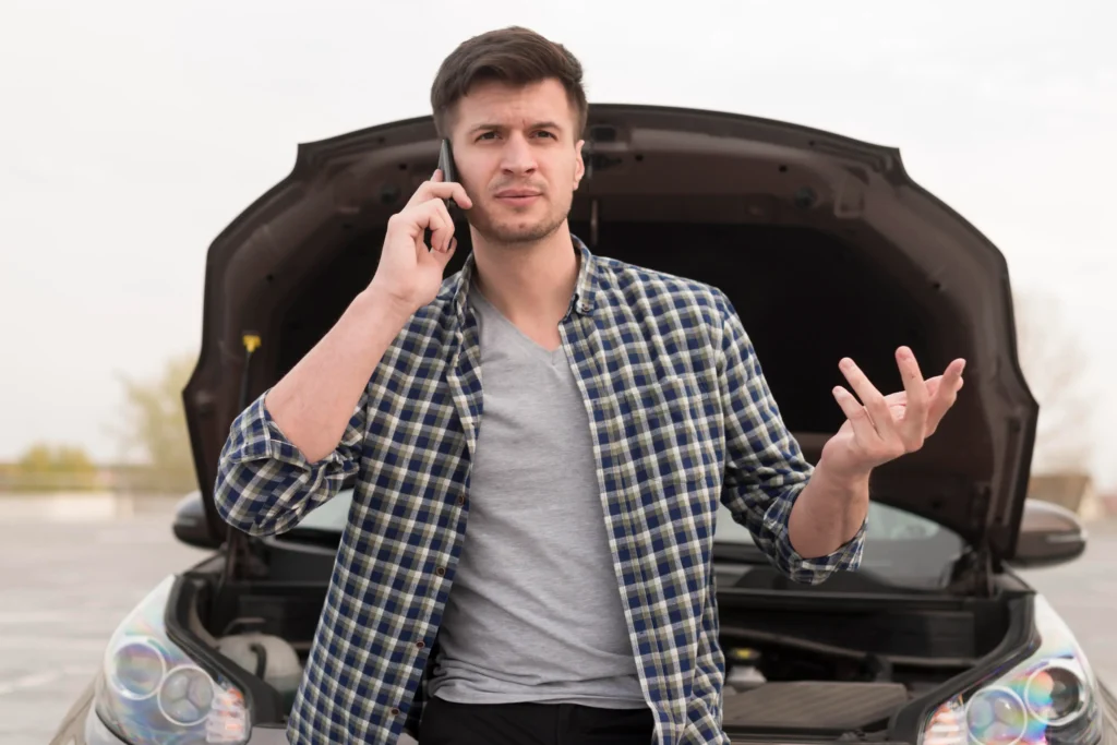 Muž stojí před otevřenou motorkou auta s mobilním telefonem.