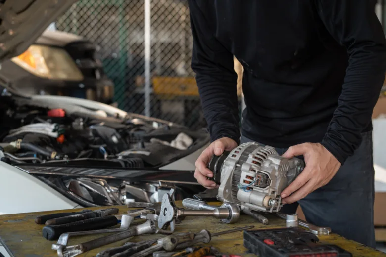 Mechanik drží automobilový alternátor u otevřeného motoru vozu.