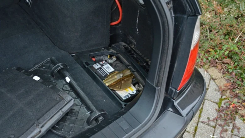 Otevřený kufr auta s vyjmutou autobaterií ležící na straně vedle plastových dílů.