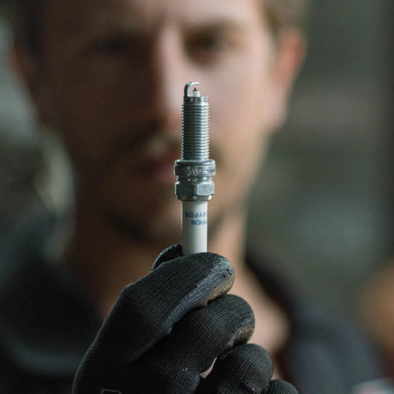 Mechanik drží zapalovací svíčku v rukavici pro kontrolu stavu.