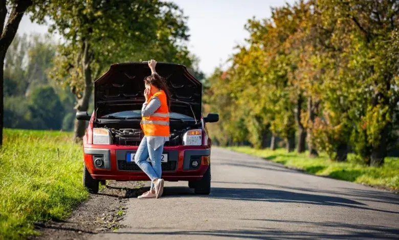 Žena u auta s otevřenou kapotou na silnici venkovské.
