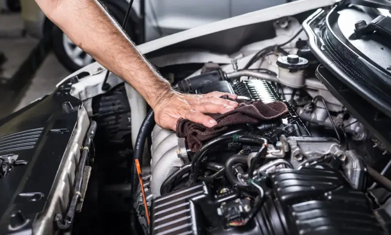 Muž čistí motor automobilu hadrem pod otevřenou kapotou.