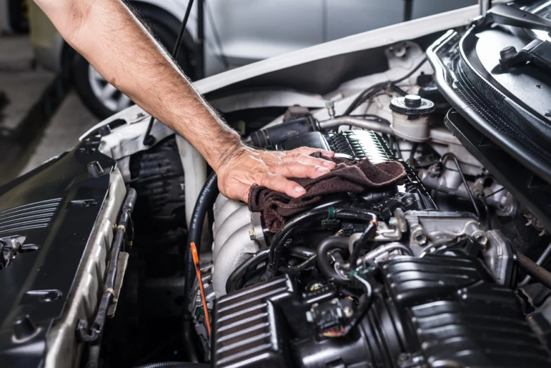 Muž čistí motor automobilu hadrem pod otevřenou kapotou.