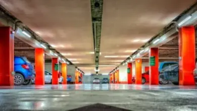 Vnitřek podzemního garáže s oranžovými sloupy a auty.