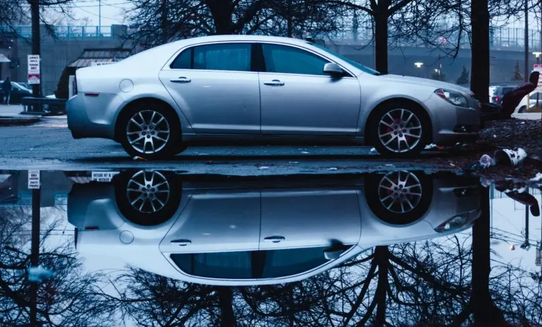 Stříbrné auto s odrazem v kaňonu na mokré silnici.