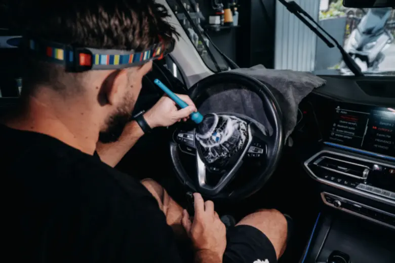 Muž čistí volant auta profesionálním nástrojem v dílně.