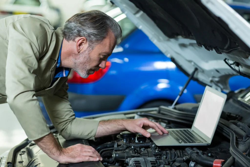 Mechanik kontroluje motor auta s notebookem v dílně.