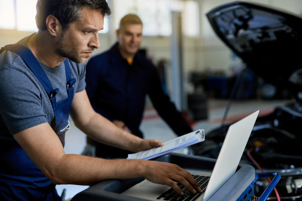 Mechanik připojuje diagnostický kabel k ECU auta v dílně s otevřenou kapotou.