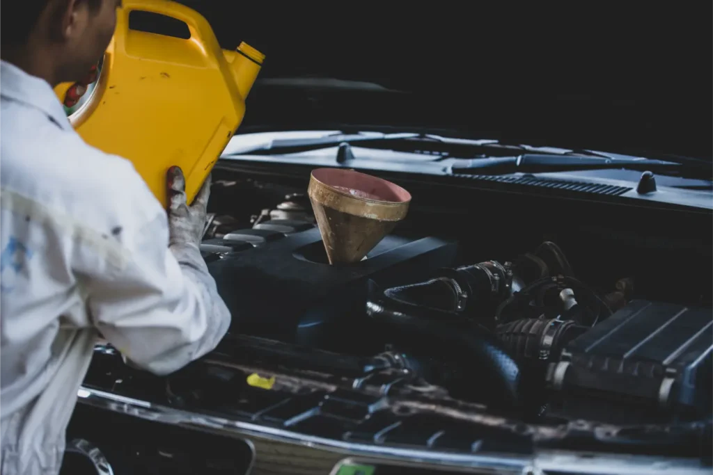 Mechanik nalévá olej do motora auta pomocí lejna.