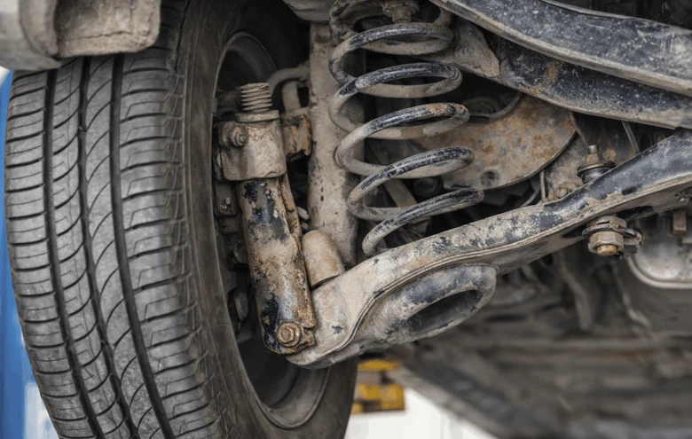 Znečištěná podvozková soustava automobilu s tlumičem a pružinou.
