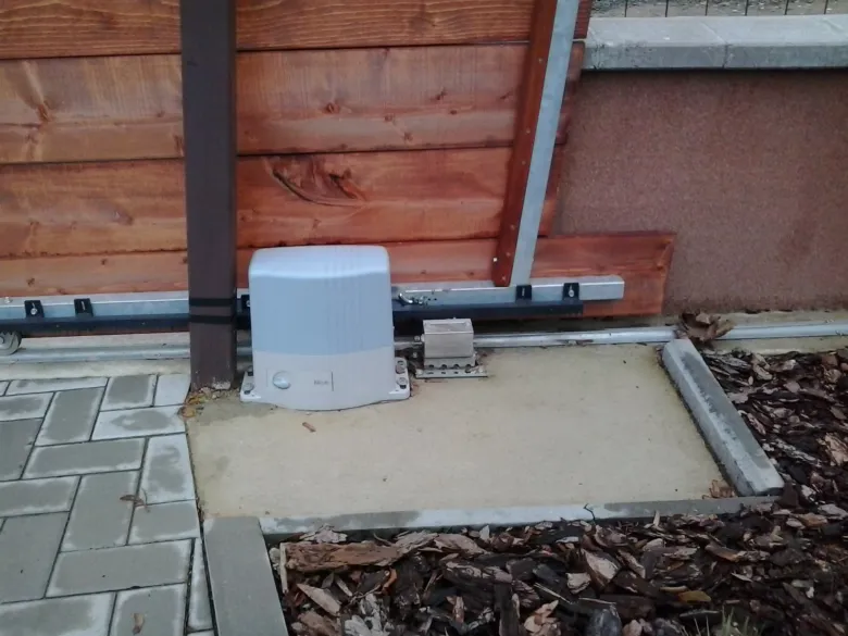 Bílý motor pro automatizaci brány u dřevěného plotu.
