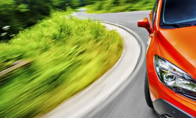Oranžový automobil jedoucí po zkrivené silnici.