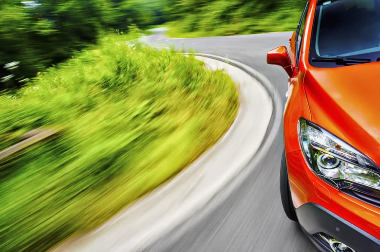 Oranžový automobil jedoucí po zkrivené silnici.