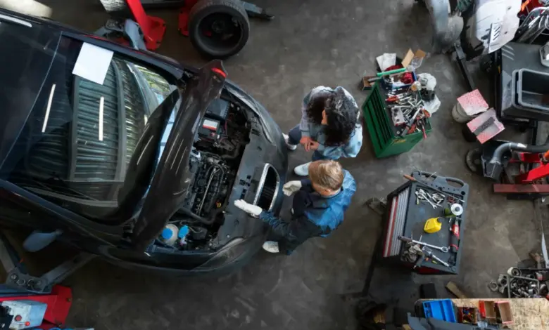 Mechanici kontrolují motor vozu v dílně s otevřenou kapotou.