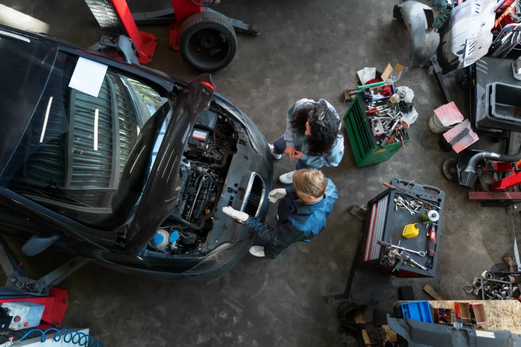 Mechanici kontrolují motor vozu v dílně s otevřenou kapotou.