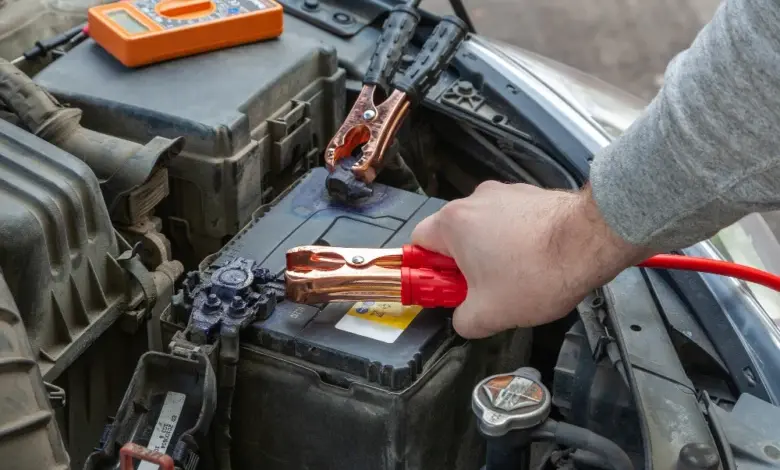 Člověk připojuje nabíjecí kabely k automobilové baterii pod kapotou.
